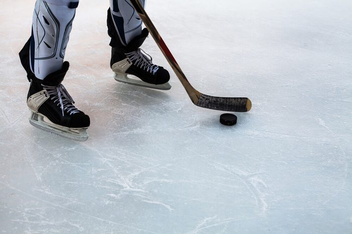 Hockey stick and puck on natural ice. Legs of hockey player.