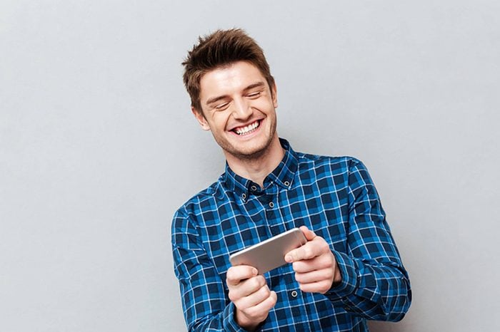 Funny man laughing while playing with smartphone isolated