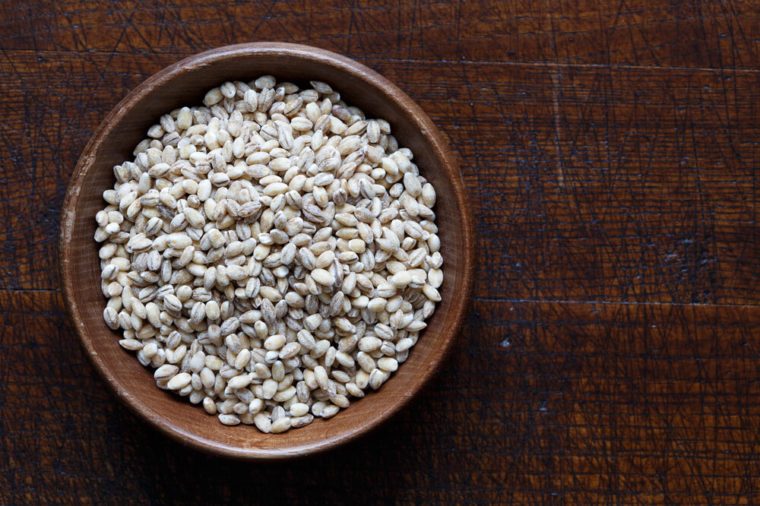 Dry pearl barley in brown wooden bowl isolated on dark wood from above.