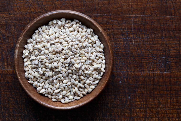 Dry pearl barley in brown wooden bowl isolated on dark wood from above.
