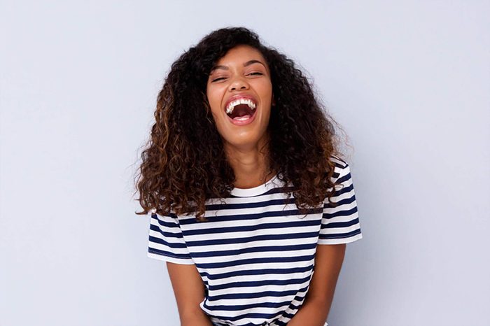 Portrait of young black woman laughing against gray wall