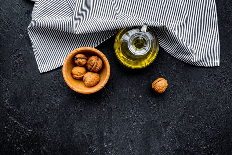 Nut oil for skin care or cooking. Walnut oil in jar near walnut in bowl on black background top view copy space