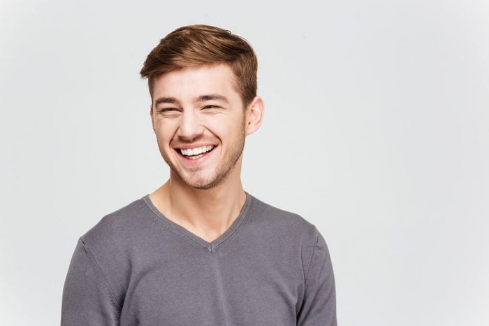 Portrait of cheerful attrative young man in grey pullover over white background