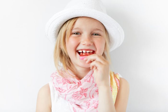 Small European girl laughing at camera and eating lollipop in white morning light. Holiday mood and cheerful atmosphere mixed with shinny white look of kid and her happy-go-lucky style.