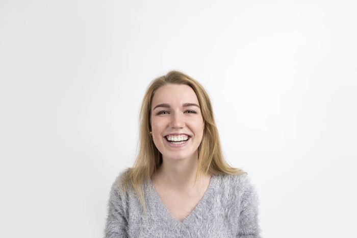 Positive blond woman in a gray sweater is smiling broadly and looking to the camera. Concept of strong positive emotions. White background. Mock up