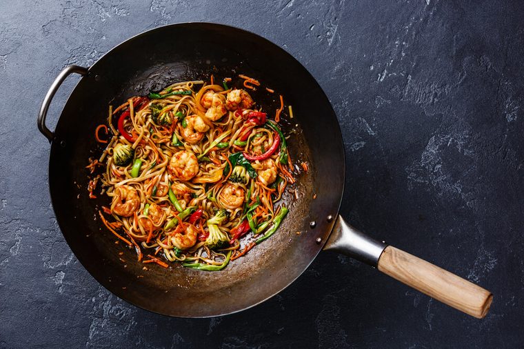 Udon stir-fry noodles with shrimp in wok pan on dark stone background
