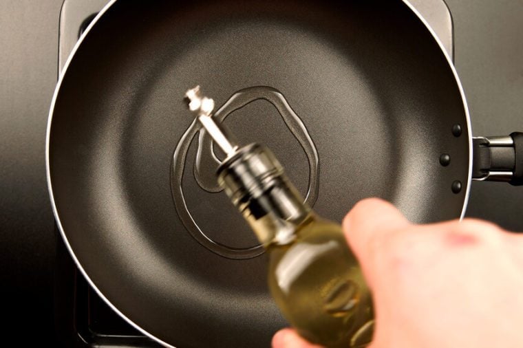 TOP VIEW: Human hands pouring olive oil on the frying pan