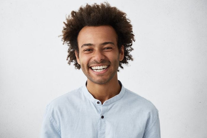 Friendly looking positive Afro American stylish man with funky hair and bristle smiling broadly during nice conversation with good old friend, standing isolated at grey studio wall. Horizontal