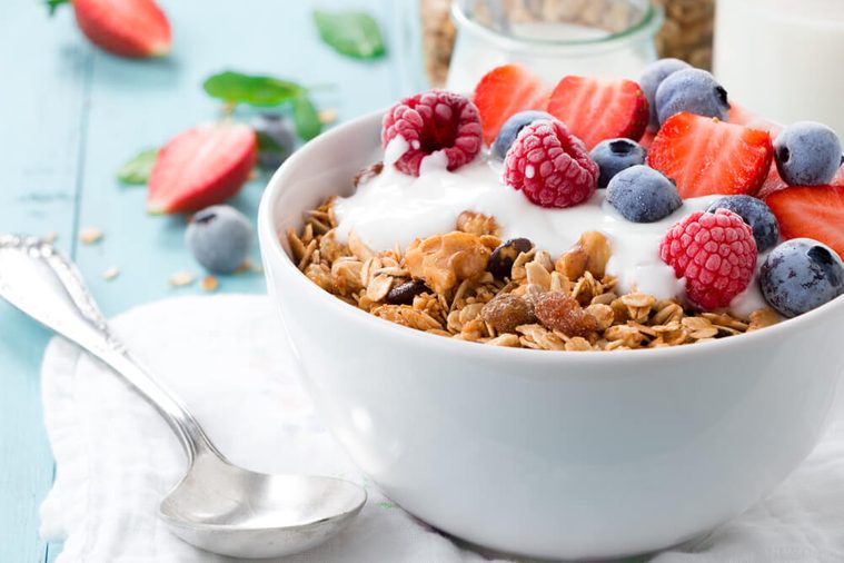 Healthy breakfast in a bowl with homemade baked granola, frozen berries, fresh strawberries and yogurt on a turquoise wooden table