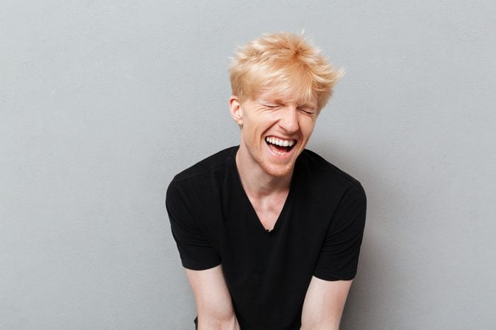 Image of caucasian man standing over grey wall near copyspace laughing.