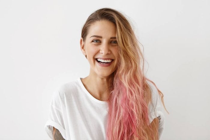 Picture of stylish trendy-looking young woman of European appearance wearing her messy pastel pink hair to the side smiling broadly, demonstrating her perfect white teeth. Youth and happiness