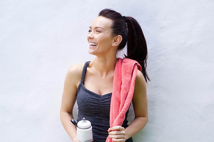 Portrait of a smiling sporty woman standing with water bottle and towel
