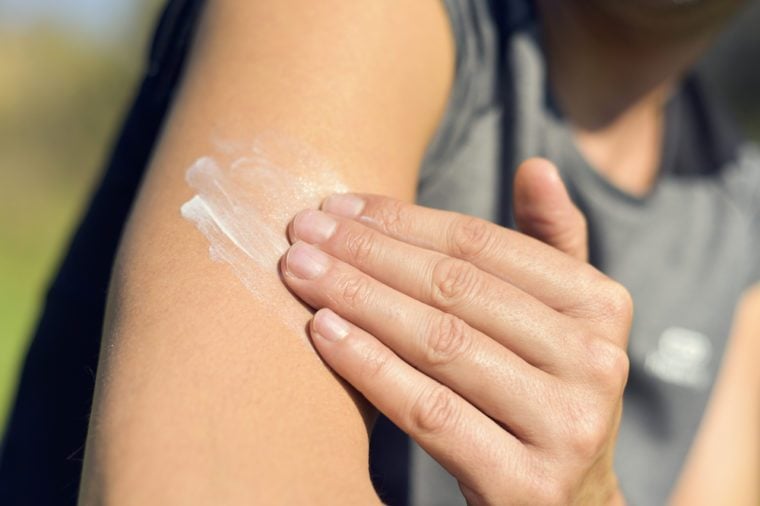 closeup of a young caucasian man wearing a T-shirt applying sunscreen to his arm