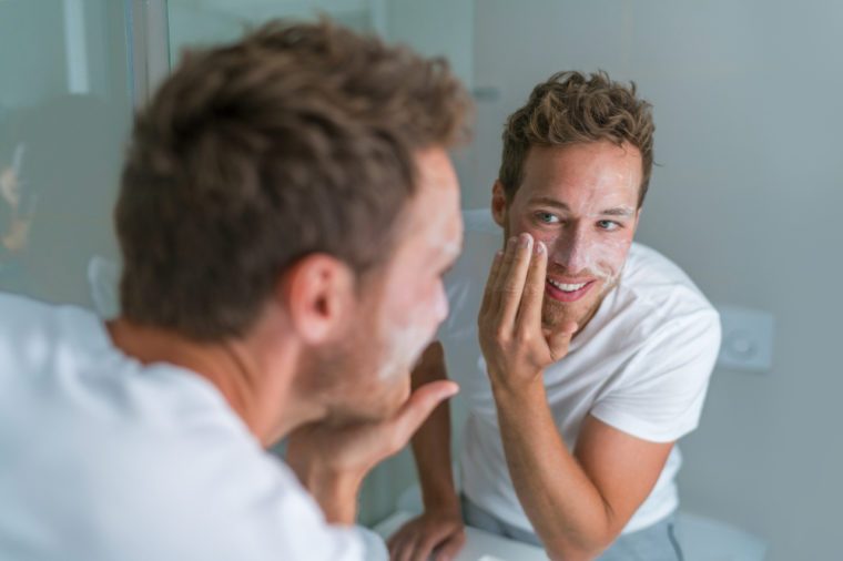 Man washing face with soap scrubbing exfoliation mask facial treatment looking in the mirror. Men taking care of skin, morning face wash routine for cleaning acne pimples.