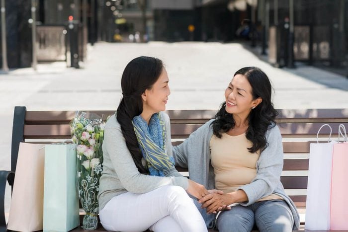Two cheerful middle-aged female friends talking while sitting on the bench
