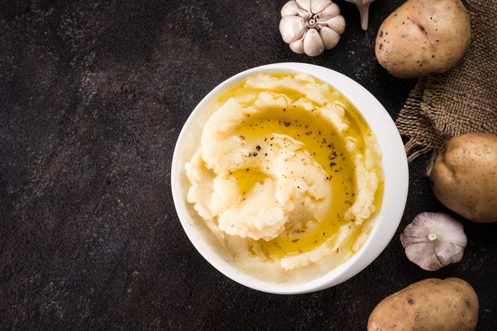 Mashed potatoes with spices and olive oil in white bowl on dark concrete background. Top view or flat lay. Copy space.