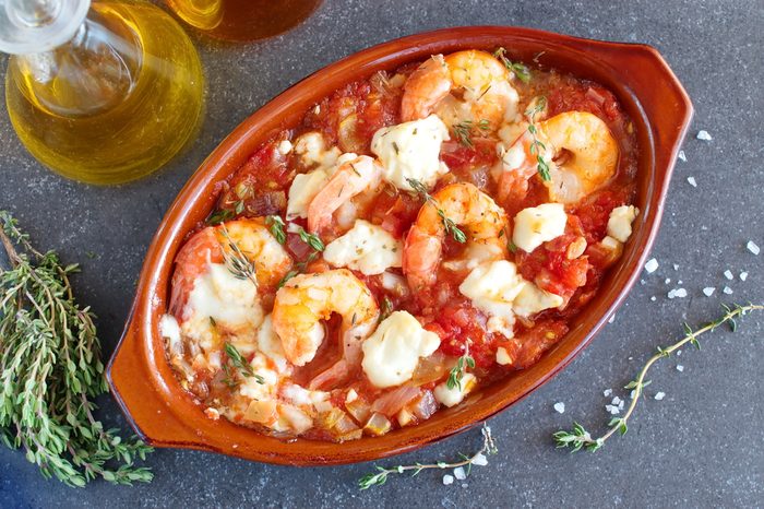 Greek traditional food. Oven backed prawns with feta, tomato, paprika, thyme in a traditional ceramic form on a abstract background. Healthy eating concept. Mediterranean lifestyle.