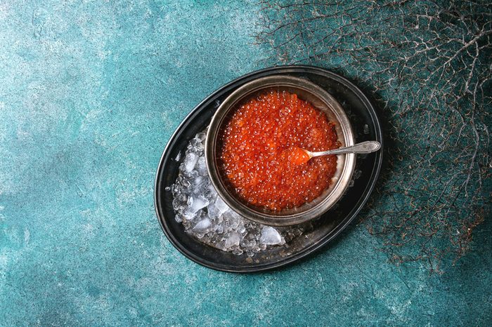 Bowl of red caviar on vintage metal tray with ice over turquoise texture background. Top view, space