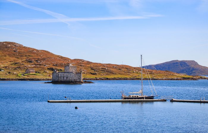 Kisimul Castle on the island of Barra, one of the outer hebrides islands and a sailing boat moored on the new marina poonton