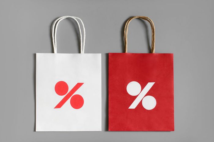Red and white shopping bags from recycle paper with percent sign on gray background. Black friday or Christmas sales.