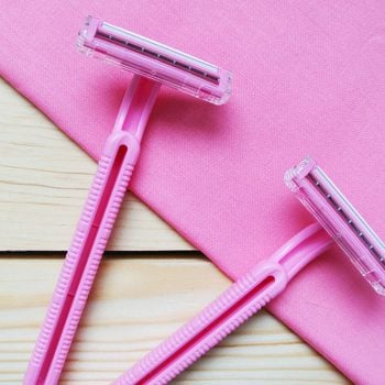 Couple of pink women's disposable razors on wooden table.