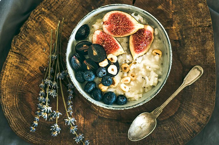 Healthy winter breakfast. Rice coconut porridge with figs, berries and hazelnuts in bowl over rustic wooden board background, top view. Clean eating, vegetarian, vegan, alkiline diet food concept