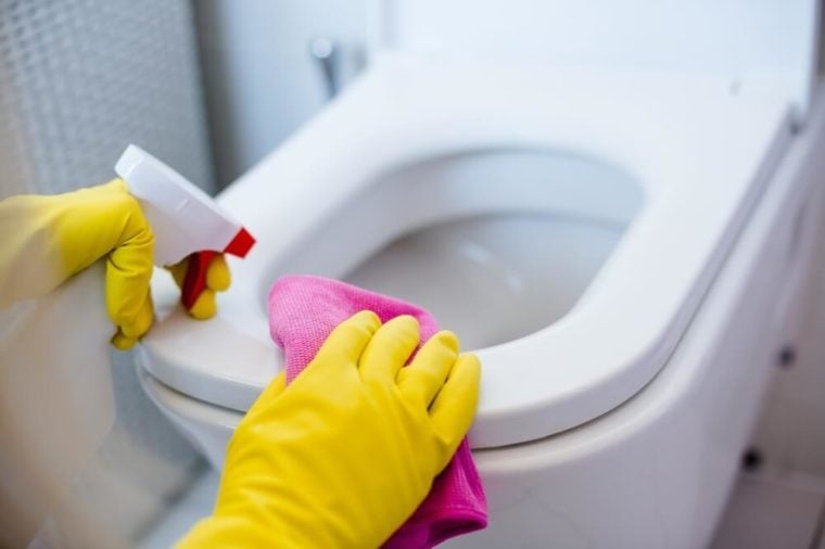 Woman in yellow rubber gloves cleaning toilet with pink cloth