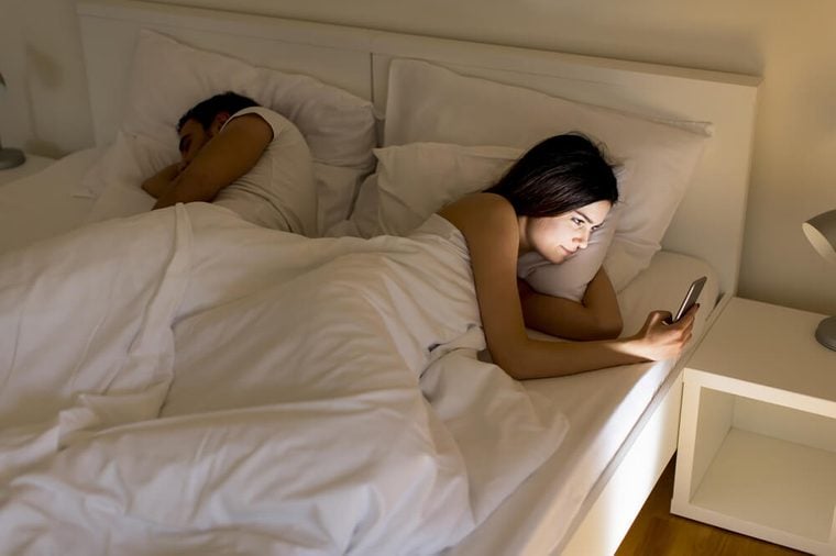 Young couple in bed. Man sleeps while a young woman looking phone at night
