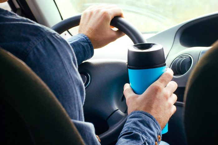 Close up of male's hand holding thermo mug with hot coffee driving in a car