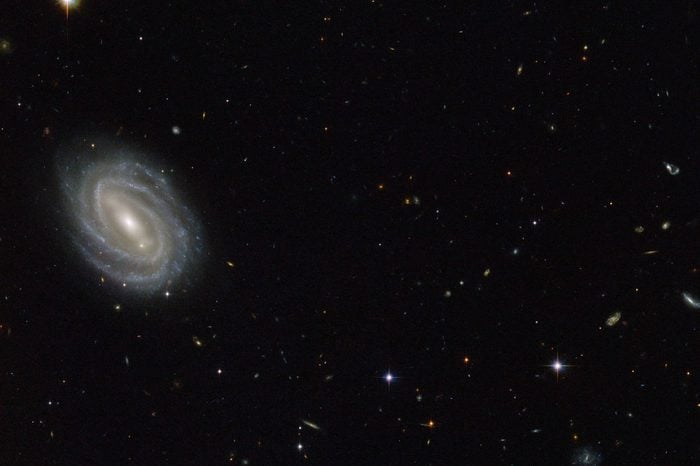 This new NASA/ESA Hubble Space Telescope image shows a beautiful spiral galaxy known as PGC 54493, located in the constellation of Serpens (The Serpent). This galaxy is part of a galaxy cluster that has been studied by astronomers exploring an intriguing phenomenon known as weak gravitational lensing. This effect, caused by the uneven distribution of matter (including dark matter) throughout the Universe, has been explored via surveys such as the Hubble Medium Deep Survey. Dark matter is one of the great mysteries in cosmology. It behaves very differently from ordinary matter as it does not emit or absorb light or other forms of electromagnetic energy — hence the term "dark." Even though we cannot observe dark matter directly, we know it exists. One prominent piece of evidence for the existence of this mysterious matter is known as the "galaxy rotation problem." Galaxies rotate at such speeds and in such a way that ordinary matter alone — the stuff we see — would not be able to hold them together. The amount of mass that is "missing" visibly is dark matter, which is thought to make up some 27 percent of the total contents of the Universe, with dark energy and normal matter making up the rest. PGC 55493 has been studied in connection with an effect known as cosmic shearing. This is a weak gravitational lensing effect that creates tiny distortions in images of distant galaxies.