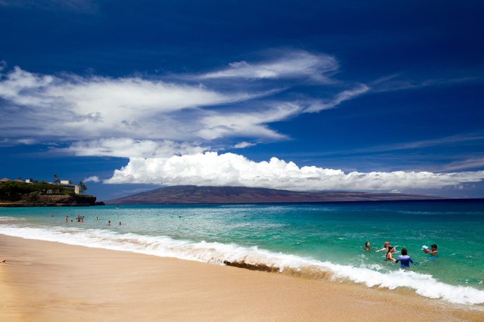 Tourists enjoying the beach at Kaanapali Beach on Maui with view towards Lanai in Hawaii, USA.