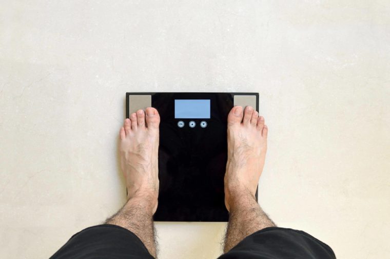 Man's view of his feet standing on a black bathroom scale