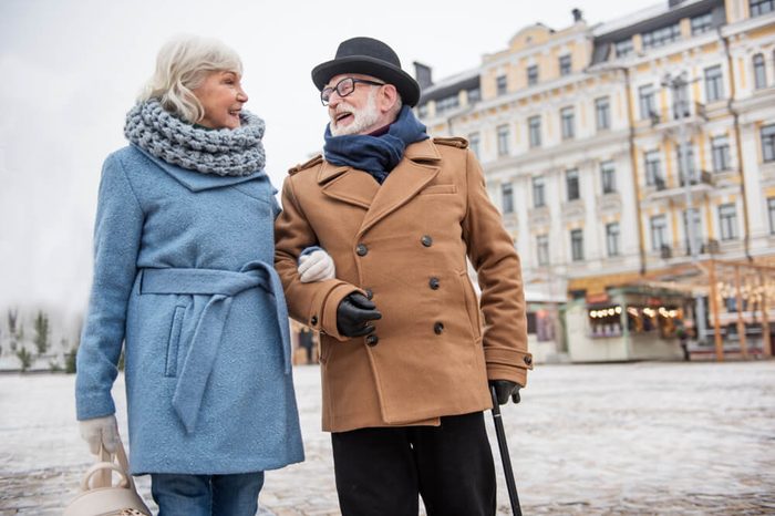 Cheerful old married couple walking arm in arm outdoor in the winter. They are talking and laughing