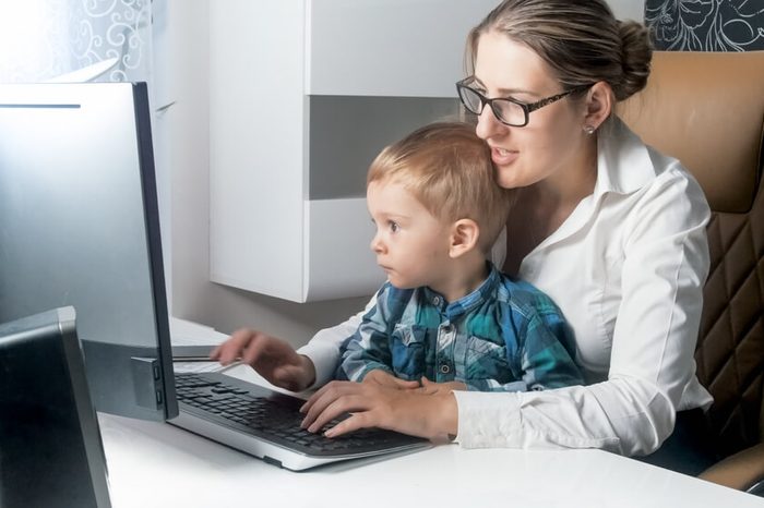 Smiling boy with mother businesswoman working in office