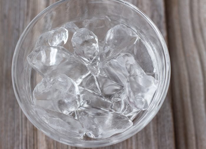 horizontal image of a clear glass bowl with ice cubes on a wooden background