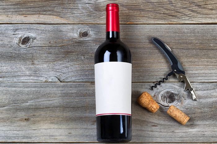 Top view angled shot of red wine bottle with corks and opener on rustic wooden boards