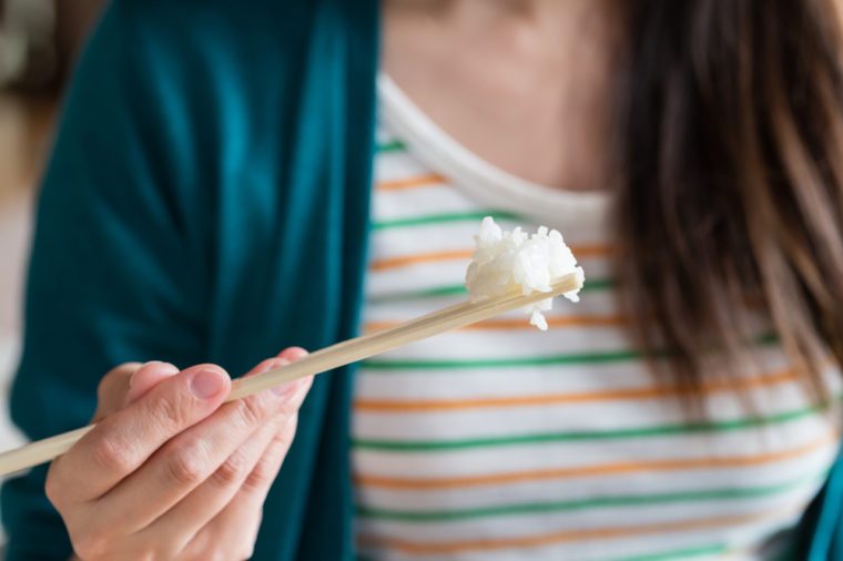 A close up of a girl eating rice with wooden chopsticks.