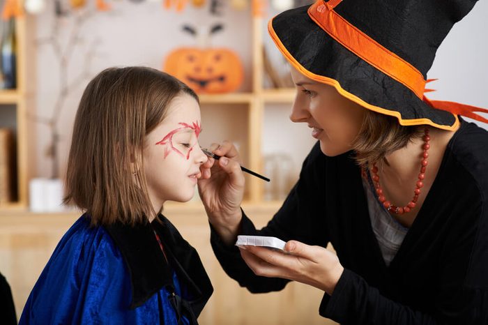 Woman applying Halloween make-up to face of her daughter