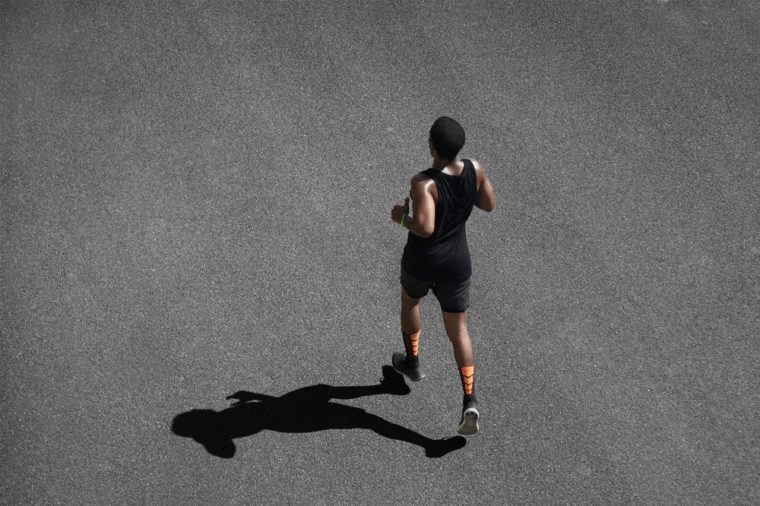 Top view of African runner wearing black sportswear training on black pavement at central position. Muscular fit sport model exercising sprint on city road. Full body length of dark-skinned sprinter