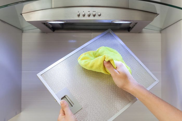 Woman Cleaning Cooker Hood With Rag In Kitchen At Home