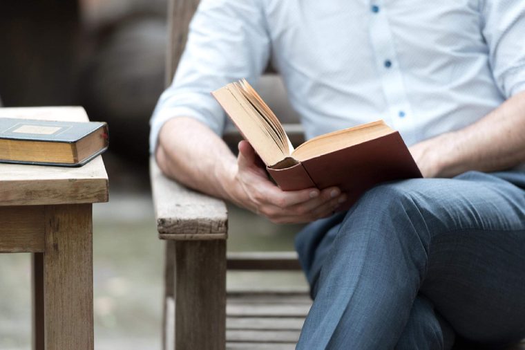Close up of a man reading a book on a chair in the park, successful people read in the morning every day.