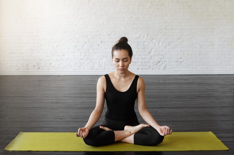 Beautiful asian young woman sitting in Lotos pose. Businesswoman practicing meditation in yoga hall after hard day, sitting in a prayer position on the green yoga mat. Time for Yoga and relaxation