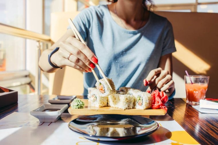 Woman in the blue shirt is eating at a sushi restaurant in summer, close-up