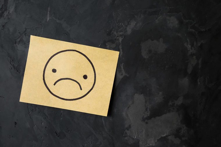 drawing of sad face on sticky note paper on cement wall texture background, loft style