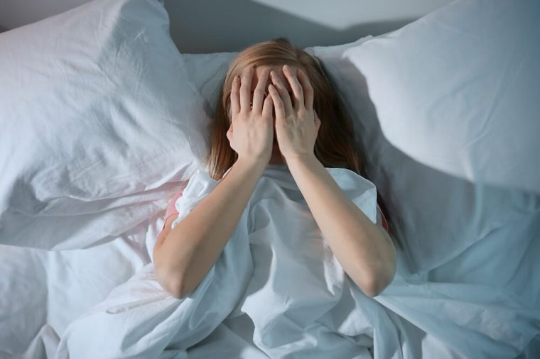 Young scared woman lying in bed at home