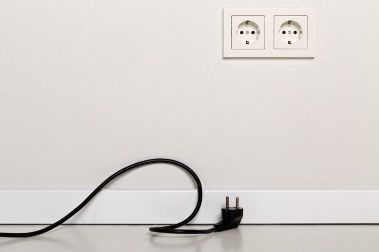 Black power cord cable unplugged with european wall outlet on white plaster wall with copy space