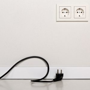Black power cord cable unplugged with european wall outlet on white plaster wall  with copy space