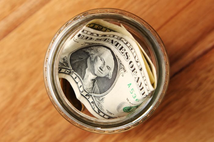 A savings jar filled with american dollars on a wooden table top. 