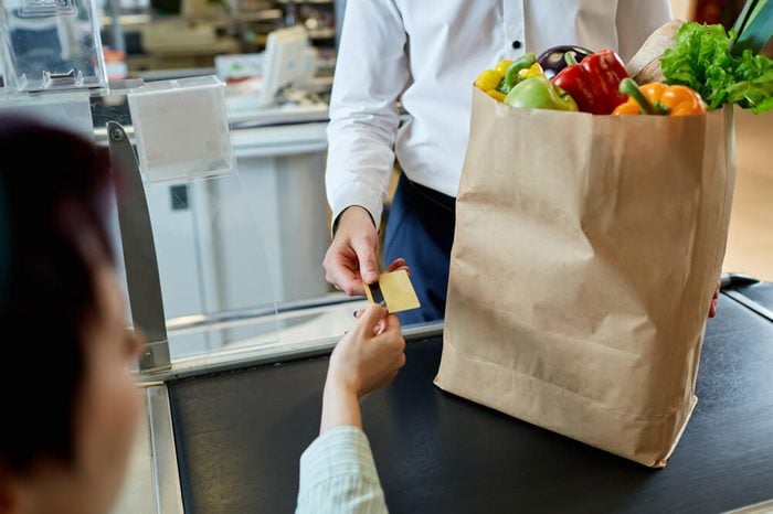 The man's hand buyer pays by card for purchase in paper bag with healthy fresh meal near cashier at the supermarket during shopping