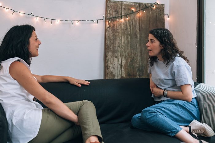 Two women friends talking to each other on a couch in apartment